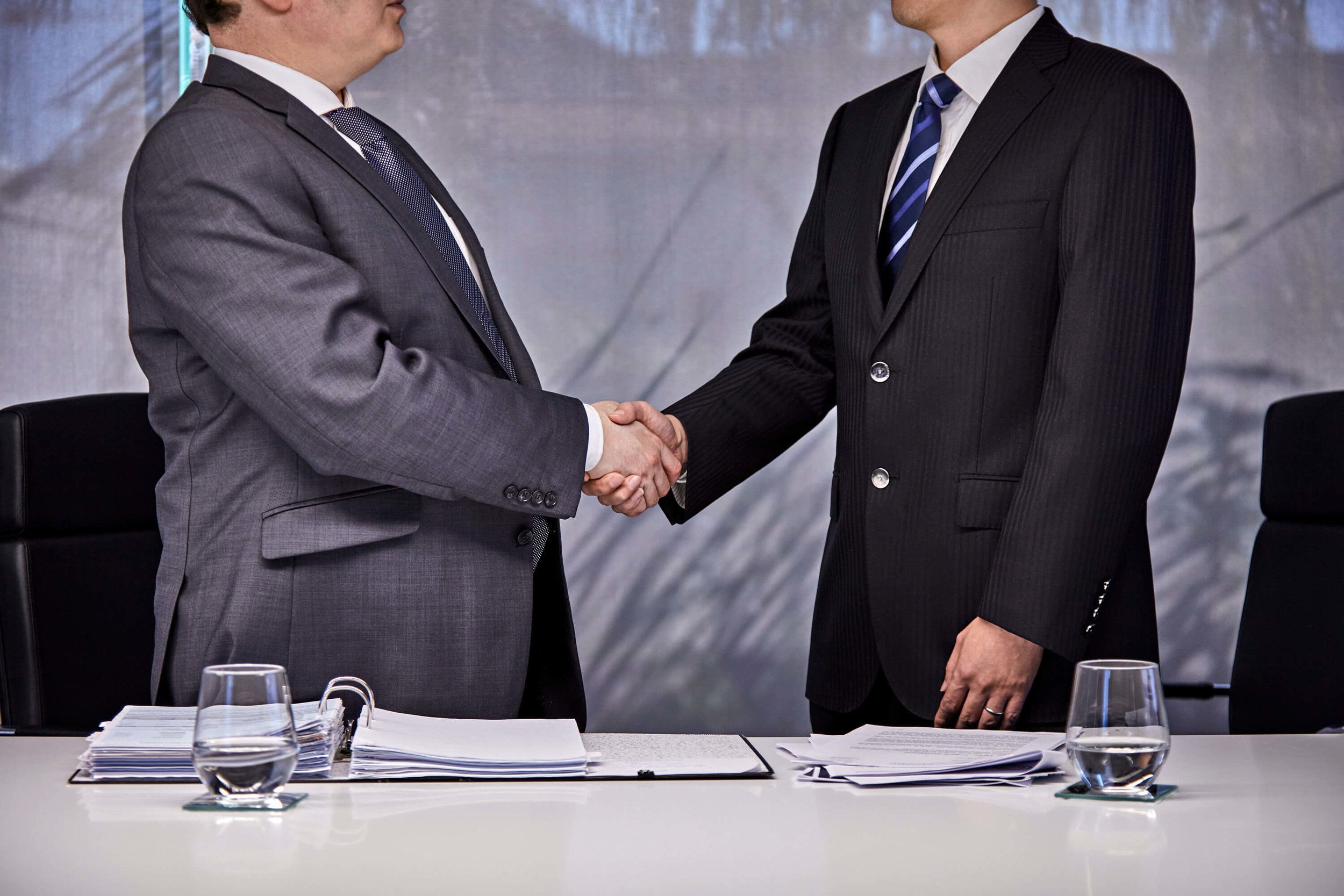 Two businessmen shaking hands across a boardroom table